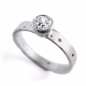 An 18ct white gold solitaire diamond engagement ring with a textured band and a central brilliant cut diamond, flanked by patterned white gold.