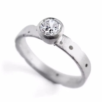 An 18ct white gold solitaire diamond engagement ring with a textured band and a central brilliant cut diamond, flanked by patterned white gold.