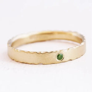 A 9ct gold engagement ring with a deep green, brilliant cut diamond set on a band with nibbled edges and a unique satin finish.