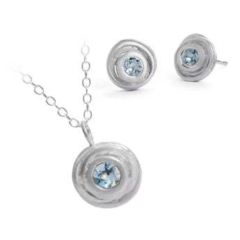 A silver pendant necklace and earring set featuring blue aquamarine gemstones in a swirling design, displayed against a white background.