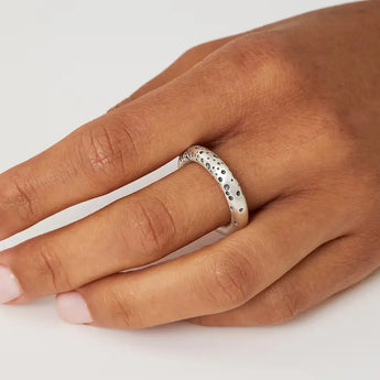A sterling silver chunky halo ring with tiny blackened holes on the band, displayed on a person's hand.