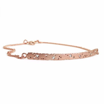 A rose gold bar bracelet with a patterned texture and small inset diamonds along its length.