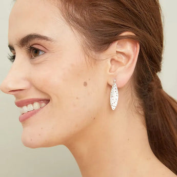 A person wearing silver leaf patterned drop earrings.