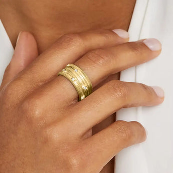 A close-up image of a person's hand wearing a wide gold ring with diamond accents on the finger.