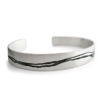 A hand etched silver cuff bracelet with oxidised patterning and a textured finish.