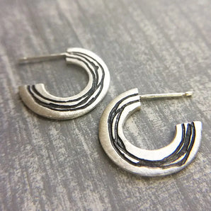 A pair of silver hoop earrings with etched patterns, displayed against a wooden background.