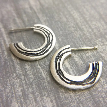 A pair of silver hoop earrings with etched patterns, displayed against a wooden background.
