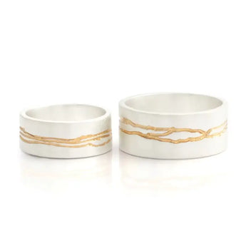 Two sterling silver wedding rings with gold detail, one larger and one smaller, set against a white background.