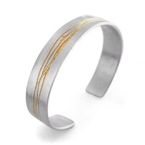 A hand etched silver and gold cuff bracelet with a textured, satin finish and a simple drawn line design.