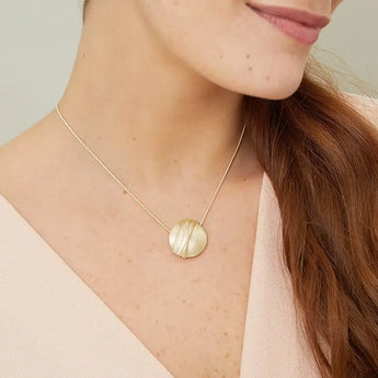 A woman wearing a gold necklace with a textured satin finish pod pendant, fastened by a T-bar style catch, with the chain appearing to float.