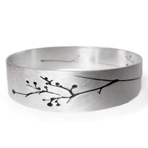 A silver bangle with floral engravings and a satin finish, displayed against a white background.