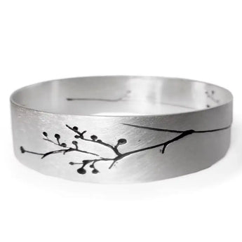 A silver bangle with floral engravings and a satin finish, displayed against a white background.