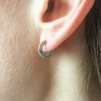 A close-up image of a person's ear wearing a silver hoop earring with a visible hand-drawn pattern.