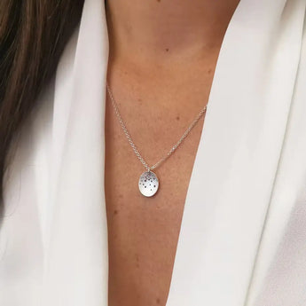 A person wearing a sterling silver oval pendant necklace with a satin finish, fastened with a bolt ring style catch. The necklace is displayed against the person's clavicle.