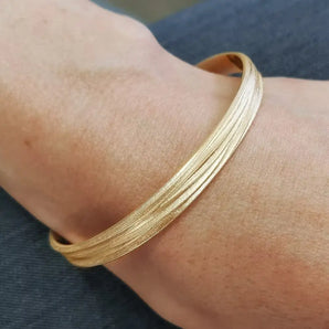 A textured gold bangle bracelet with a frosted finish worn on a person's wrist.
