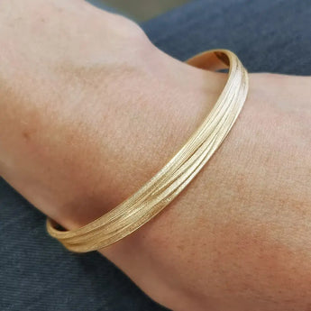 A textured gold bangle bracelet with a frosted finish worn on a person's wrist.