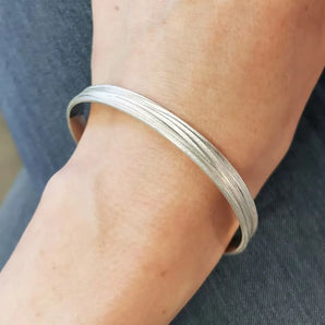 A silver bangle bracelet with a textured matte finish worn on a person's wrist.