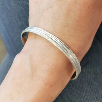 A silver bangle bracelet with a textured matte finish worn on a person's wrist.
