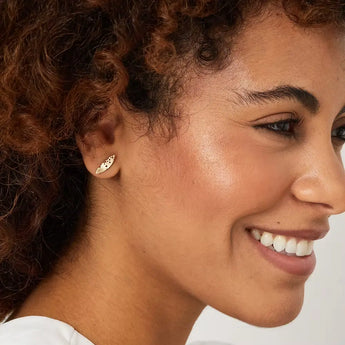 A person wearing patterned gold leaf earrings with a smile on their face.