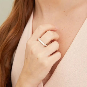 A silver ring with a patterned halo design, worn on a person's finger.