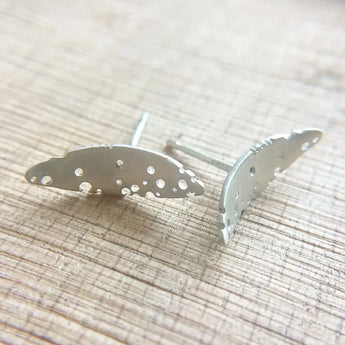 A pair of patterned silver leaf-shaped earrings displayed on a wooden surface.