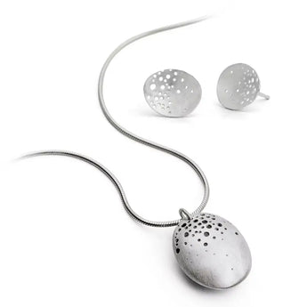 A silver necklace with a hand-drilled hollow pod pendant accompanied by a pair of dome earrings, displayed against a white background.