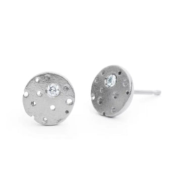 A pair of silver earrings with a frosted texture and central brilliant cut diamond, set in a circular design with burnished edges and a stud fitting.
