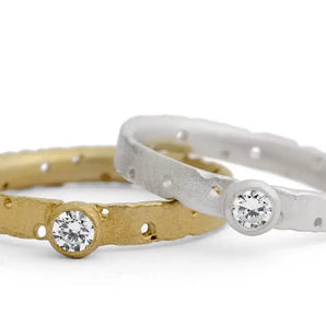 Two solitaire diamond engagement rings, one with a textured gold band and the other with a frosted silver band, each featuring a brilliant cut diamond.