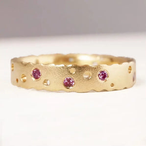A 9ct yellow gold eternity ring with patterned texture and pink brilliant cut diamonds set in it.