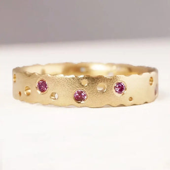 A 9ct yellow gold eternity ring with patterned texture and pink brilliant cut diamonds set in it.