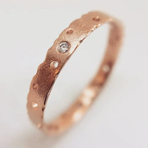 A 9ct rose gold engagement ring with a central ethically sourced diamond, featuring delicate detailing and organic nibbled edges.
