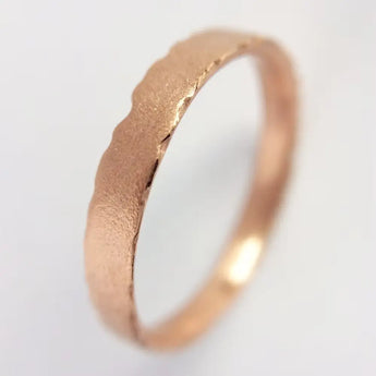 A 9ct rose gold wedding ring with nibbled edges on a white background.