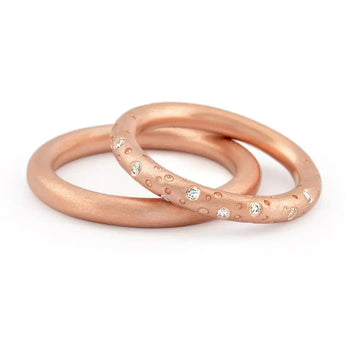 A set of two rose gold eternity rings, one with a pattern of drilled holes and set with brilliant cut diamonds, and a plain ring next to it.