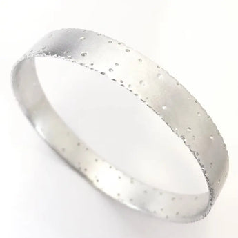 A silver bangle bracelet with a frosted finish and nibbled edges, displayed against a white background.
