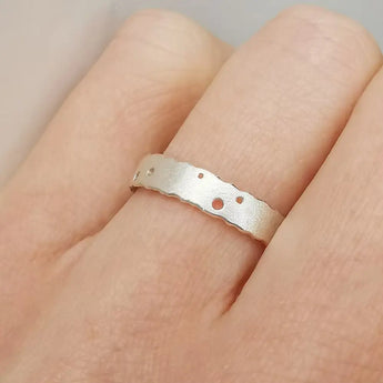 A silver ring with a textured satin finish and burnished edges, featuring a nibbled pattern, worn on a person's finger.