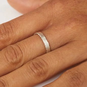 A close-up image of a person's hand showcasing a sterling silver ring with nibbled edges on the finger.