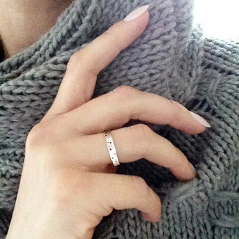 A person's hand wearing a slim silver ring with patterning, resting on a grey knitted surface.