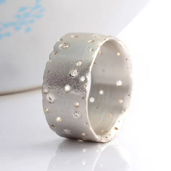A sterling silver wide band eternity ring with a patterned design and scattered brilliant cut diamonds set against a frosted finish.
