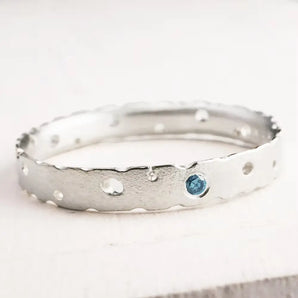 A sterling silver engagement ring with a frosted satin finish and a blue diamond gemstone, displayed against a white background.