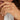 A close-up image of a person's hand wearing a slim gold wedding ring with texture reminiscent of windswept sand dunes.