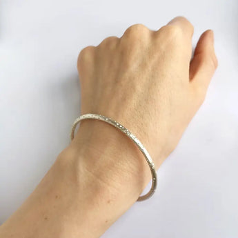 A silver bangle with a patterned design displayed on a person's wrist.
