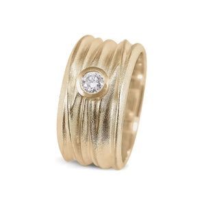 A gold wide band solitaire ring with a round brilliant cut diamond set in the center, featuring a textured pattern on the outside and a smooth interior.