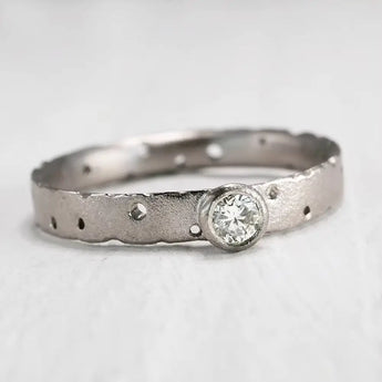 A textured 9ct white gold diamond engagement ring with a brilliant cut center stone and patterned band.