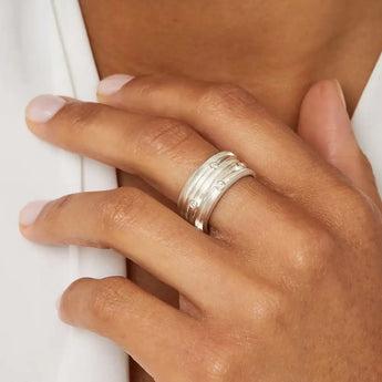 A person's hand showcasing a wide silver ring with scattered diamonds on a finger.