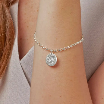 A silver plated bracelet with patterned detail and a polished letter, displayed on a person's wrist.