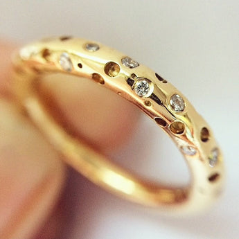 Gold ring with embedded diamonds held by a hand against a neutral background