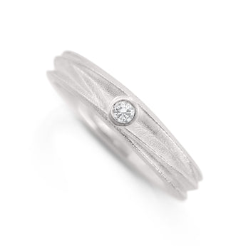 Textured silver band featuring a centrally positioned round diamond set into the surface of the ring