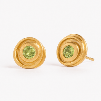 A pair of gold spiral stud earrings with round green Peridot gemstones in the center, displayed on a clean white background.
