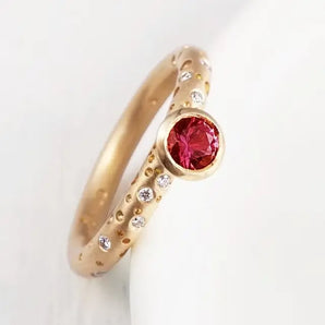 An 18ct gold engagement ring featuring a central ruby gem surrounded by smaller diamond accents.