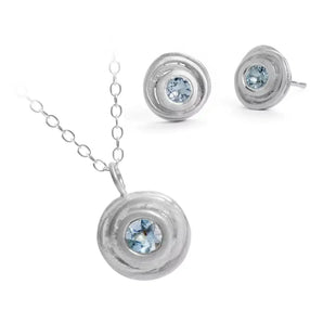A silver pendant necklace and earring set featuring blue aquamarine gemstones in a swirling design, displayed against a white background.
